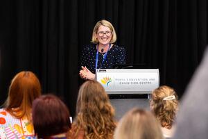 A presenter at a lectern presenting to rows of attendees