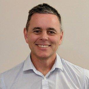 Headshot of Professor David Trembath. David wears a button up shirt and is smiling at the camera.