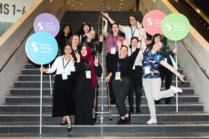 2024 Student volunteers posing on stairs, holding four large lollipops sign and throwing arms in the air