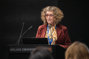 A presenter at a lectern presenting to attendees